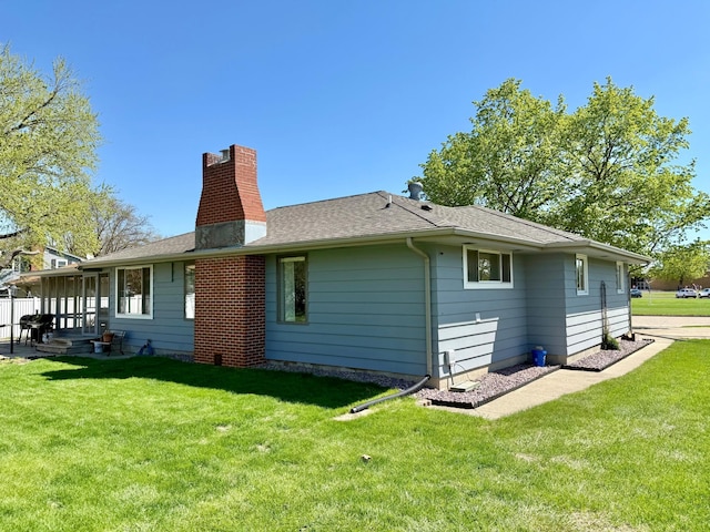 back of house featuring a yard, a chimney, and a shingled roof