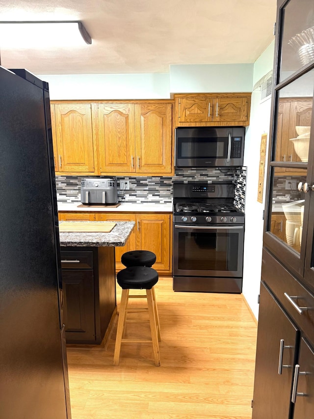 kitchen with gas range oven, stainless steel microwave, freestanding refrigerator, light wood-style flooring, and tasteful backsplash