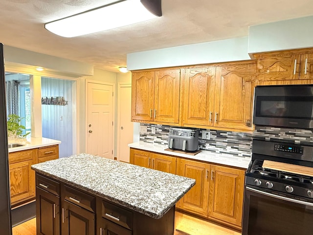 kitchen with black gas range oven, decorative backsplash, light wood-style floors, brown cabinetry, and a kitchen island