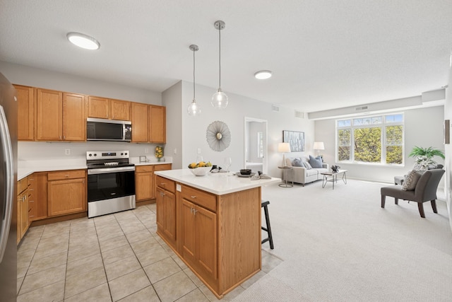 kitchen featuring appliances with stainless steel finishes, open floor plan, light countertops, hanging light fixtures, and a center island