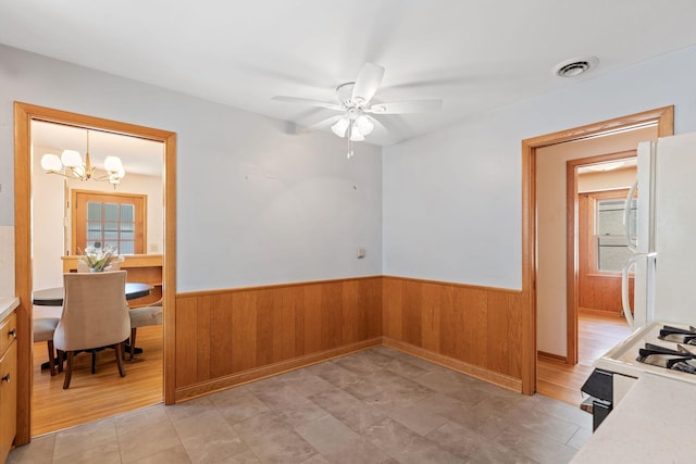 unfurnished dining area with wainscoting, a chandelier, wooden walls, and a ceiling fan