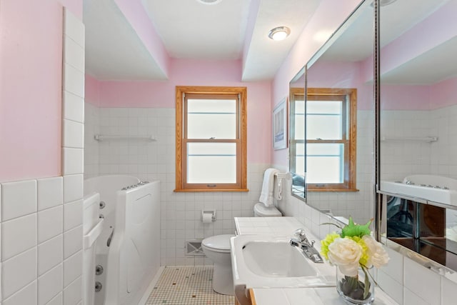 bathroom featuring tile walls, tile patterned floors, toilet, wainscoting, and a bath