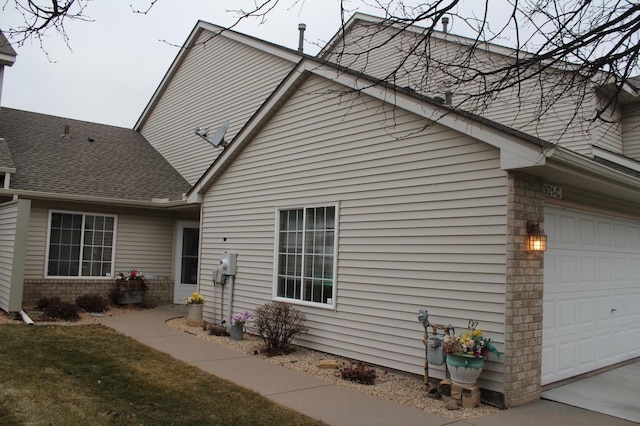rear view of house featuring a garage, roof with shingles, and brick siding