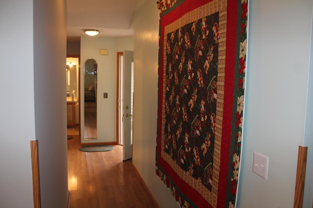 corridor with wood finished floors, arched walkways, and baseboards