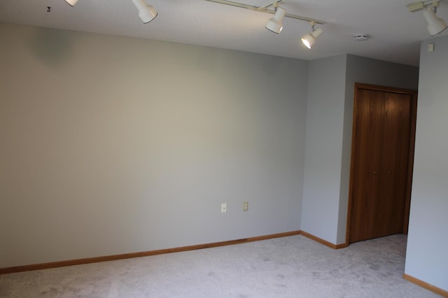 spare room featuring light colored carpet, rail lighting, baseboards, and a smoke detector