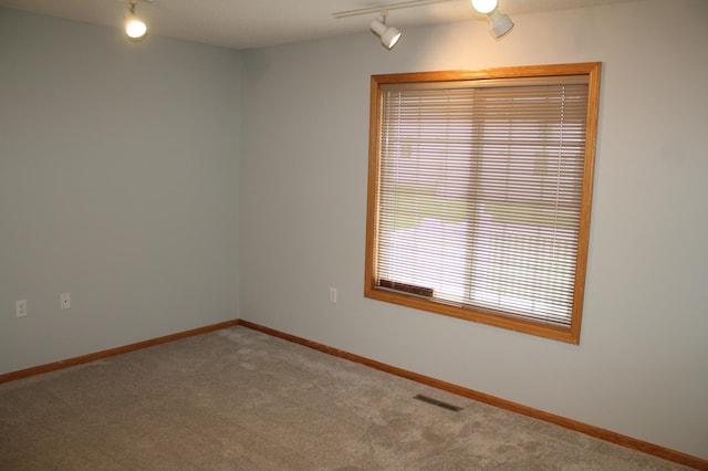 carpeted empty room featuring rail lighting and baseboards