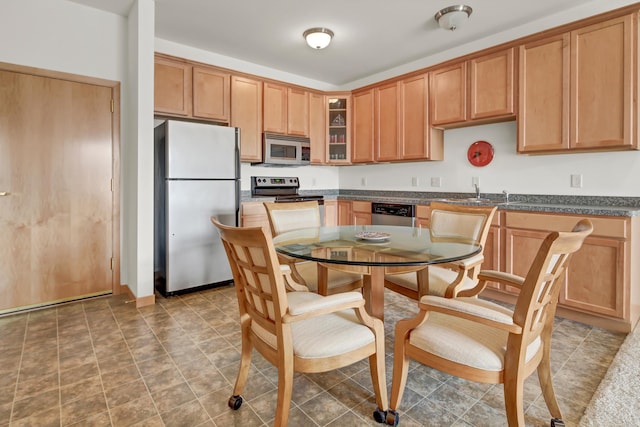 kitchen with stainless steel appliances, dark countertops, glass insert cabinets, and a sink