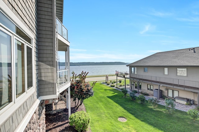 view of green lawn with a water view, cooling unit, and a balcony