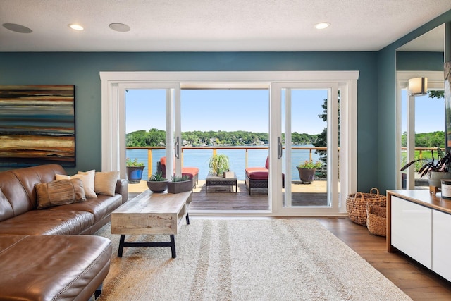 living room featuring plenty of natural light, wood finished floors, recessed lighting, a water view, and a textured ceiling