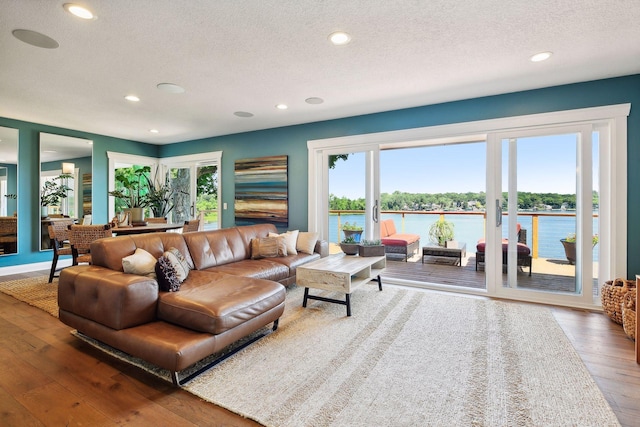 living room featuring recessed lighting, hardwood / wood-style flooring, a textured ceiling, healthy amount of natural light, and a water view