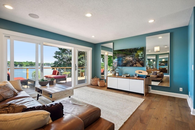 living room featuring a water view, a textured ceiling, wood-type flooring, recessed lighting, and baseboards
