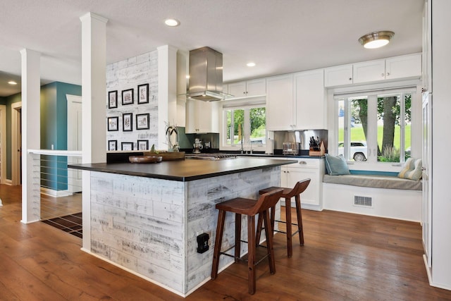 kitchen with island exhaust hood, dark countertops, dark wood-style floors, white cabinets, and a breakfast bar