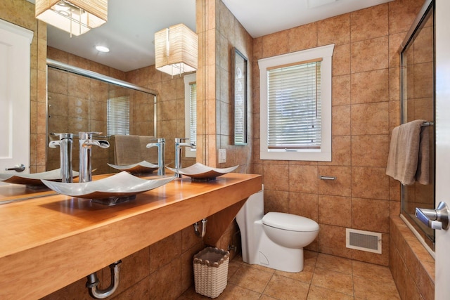 bathroom featuring tile walls, tile patterned floors, a sink, a tile shower, and toilet