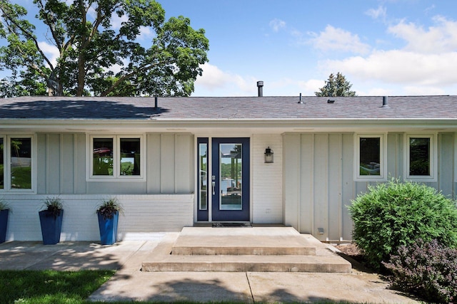 property entrance featuring board and batten siding, brick siding, and a shingled roof