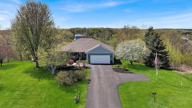 single story home with driveway, a front lawn, a garage, and a wooded view