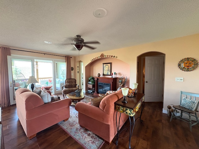 living room featuring arched walkways, a textured ceiling, wood finished floors, ceiling fan, and a glass covered fireplace