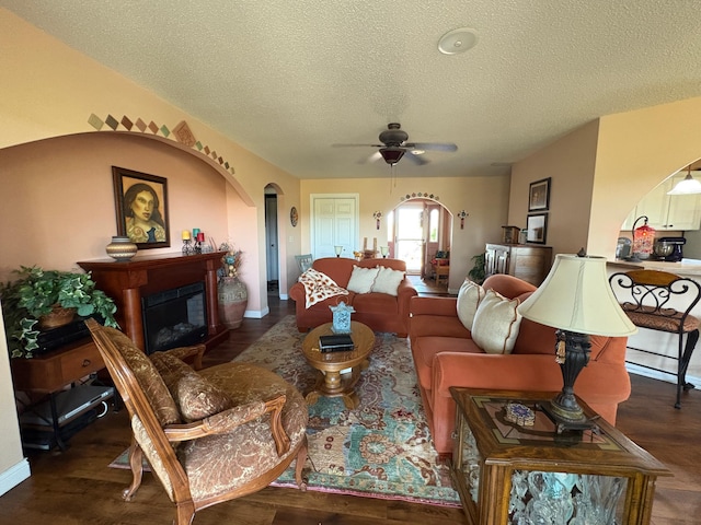 living room with arched walkways, a textured ceiling, ceiling fan, a fireplace, and wood finished floors