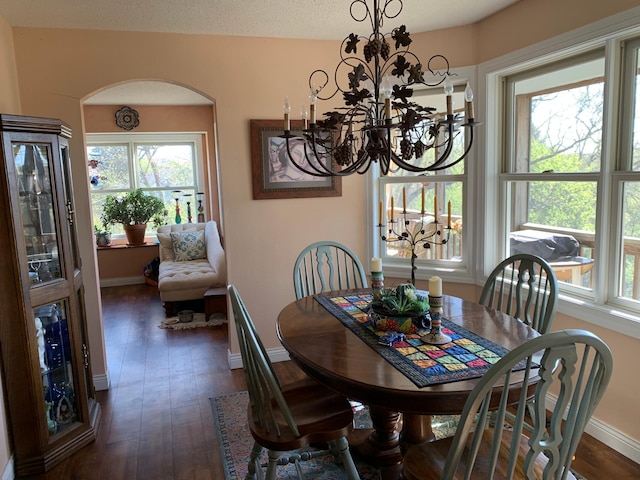 dining space featuring arched walkways, a chandelier, dark wood finished floors, and baseboards
