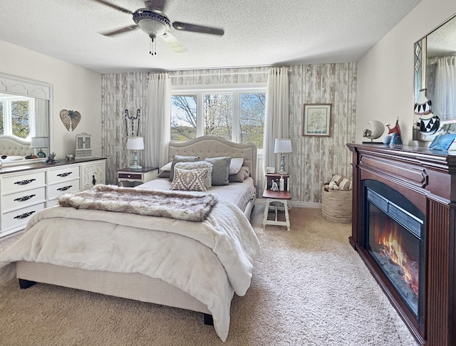 bedroom featuring multiple windows, carpet floors, a textured ceiling, a glass covered fireplace, and a ceiling fan