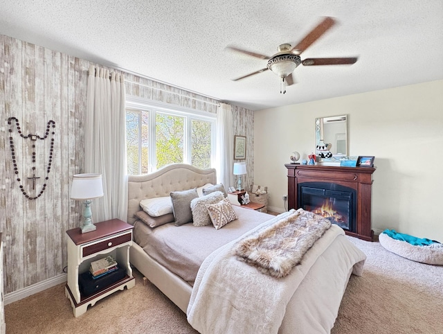 bedroom with carpet floors, a textured ceiling, a glass covered fireplace, baseboards, and ceiling fan
