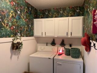 laundry room with cabinet space, wallpapered walls, and washing machine and clothes dryer