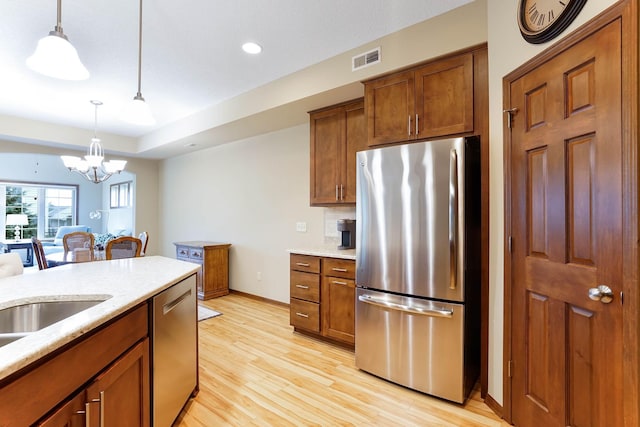 8713 9th Pl N, Lake Elmo, MN 55042 - kitchen featuring appliances with stainless steel finishes, light wood-style flooring, pendant lighting, a chandelier, and brown cabinetry