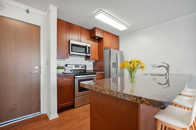 kitchen with stainless steel appliances, ornamental molding, a sink, a peninsula, and a breakfast bar area