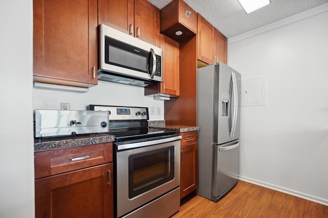 kitchen with appliances with stainless steel finishes, light wood finished floors, brown cabinetry, ornamental molding, and baseboards