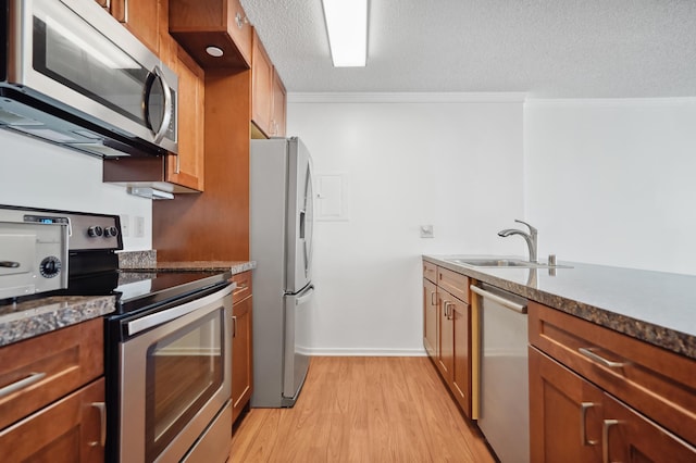 kitchen with appliances with stainless steel finishes, light wood-style floors, brown cabinets, crown molding, and a sink