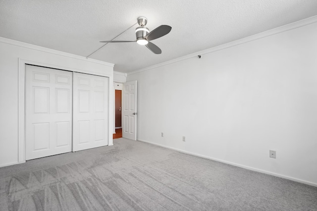 unfurnished bedroom with ornamental molding, carpet, a closet, a textured ceiling, and a ceiling fan