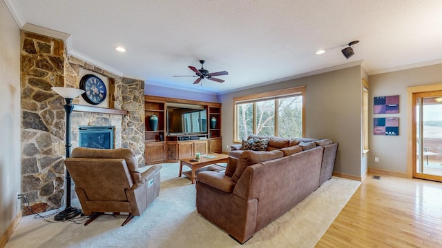 living room featuring crown molding, baseboards, a stone fireplace, light wood-style flooring, and ceiling fan
