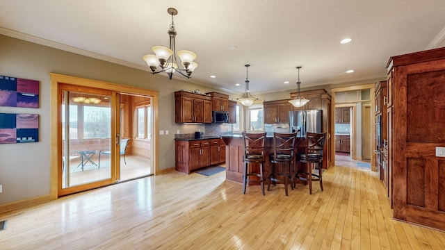kitchen featuring appliances with stainless steel finishes, a chandelier, crown molding, light wood-style floors, and a breakfast bar area