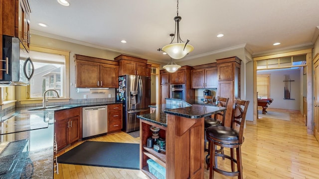 kitchen with appliances with stainless steel finishes, a sink, light wood-style flooring, ornamental molding, and a kitchen island