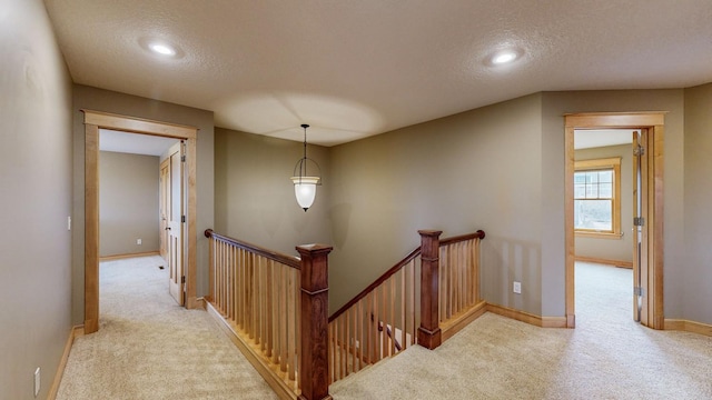 corridor featuring an upstairs landing, carpet flooring, a textured ceiling, baseboards, and recessed lighting