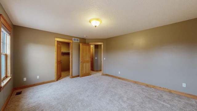 unfurnished bedroom with light colored carpet, baseboards, a spacious closet, a closet, and a textured ceiling