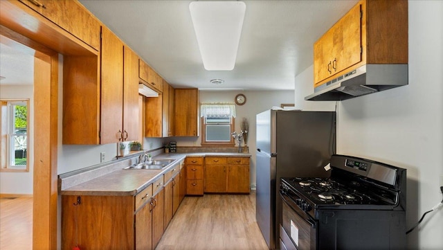 kitchen with appliances with stainless steel finishes, under cabinet range hood, a sink, light wood-style floors, and brown cabinets