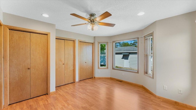 unfurnished bedroom featuring multiple closets, light wood finished floors, a textured ceiling, baseboards, and a ceiling fan