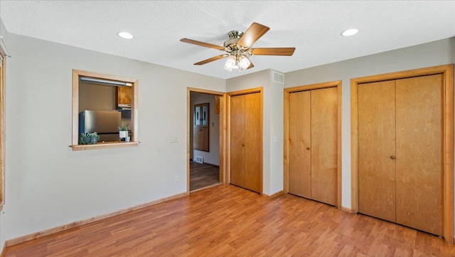 unfurnished bedroom with freestanding refrigerator, multiple closets, wood finished floors, baseboards, and recessed lighting