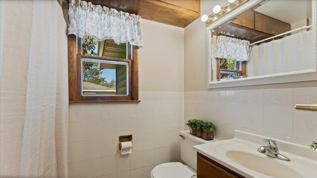 bathroom with toilet, tile walls, vanity, a shower with shower curtain, and wainscoting