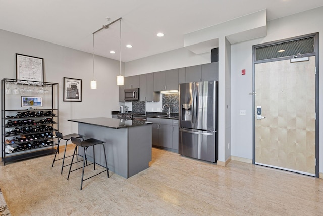 kitchen featuring stainless steel appliances, dark countertops, a sink, gray cabinets, and a breakfast bar