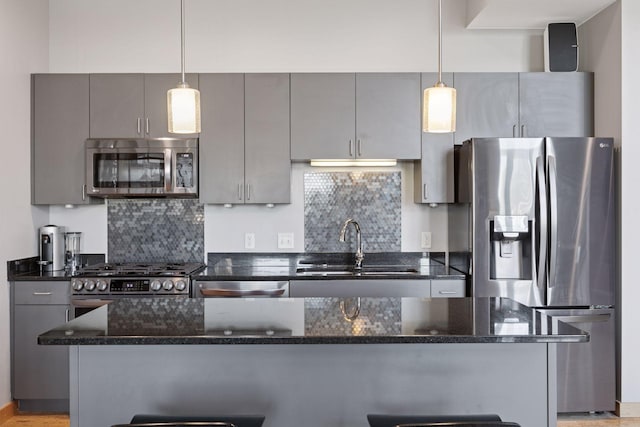 kitchen featuring appliances with stainless steel finishes, a sink, gray cabinetry, a center island, and tasteful backsplash