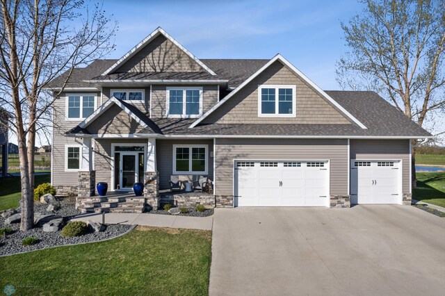 craftsman-style house with concrete driveway, roof with shingles, a front yard, stone siding, and a garage