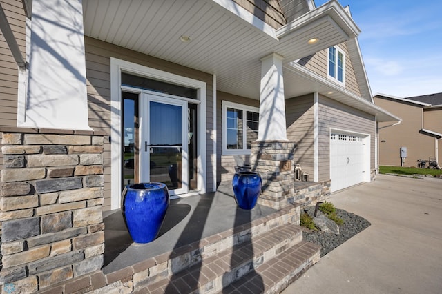 property entrance with concrete driveway, covered porch, a garage, and stone siding
