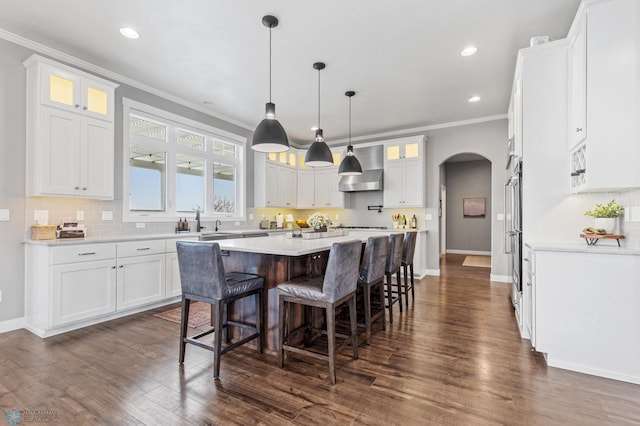 kitchen with arched walkways, ornamental molding, a kitchen island, white cabinets, and a breakfast bar area