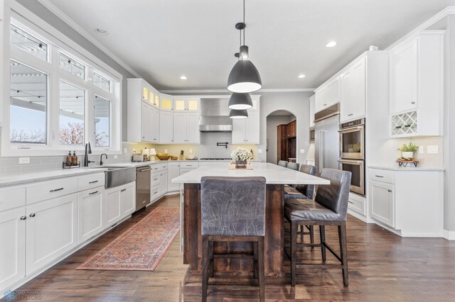 kitchen with appliances with stainless steel finishes, ornamental molding, arched walkways, a breakfast bar, and dark wood-style floors