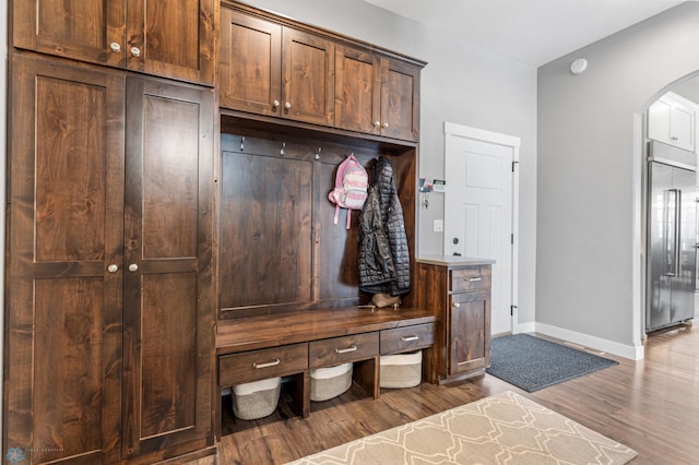 mudroom with arched walkways, wood finished floors, and baseboards