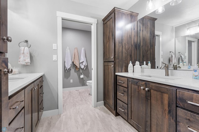 full bathroom featuring two vanities, toilet, and baseboards