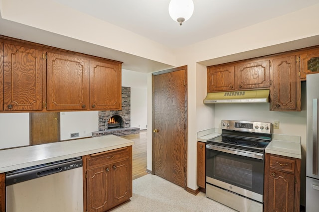 3529 Jerry St, White Bear Lake, MN 55110 - kitchen with appliances with stainless steel finishes, under cabinet range hood, light countertops, a fireplace, and brown cabinetry