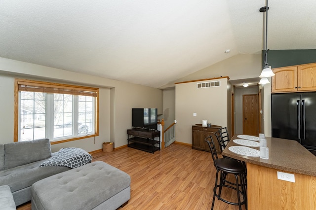living room featuring lofted ceiling, light wood-style floors, and baseboards