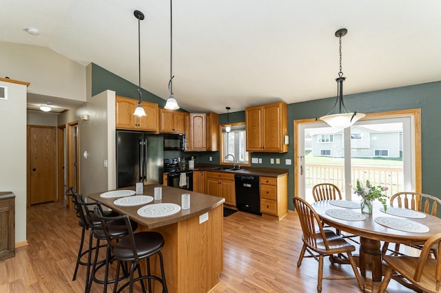 kitchen with black appliances, a sink, vaulted ceiling, light wood-style floors, and dark countertops
